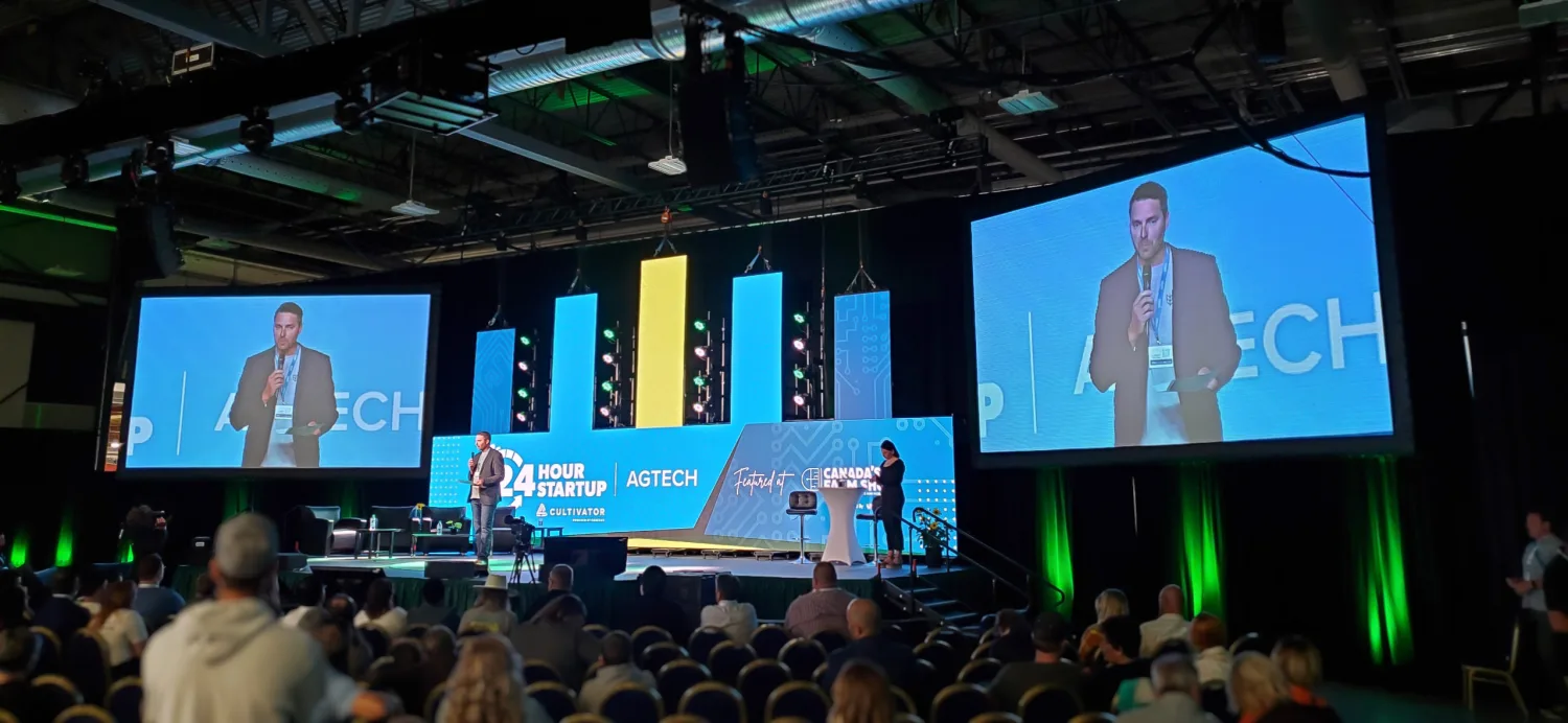 A general session with a speaker on IMAG screens either side of a stage LED wall, lit and running in front of a full room